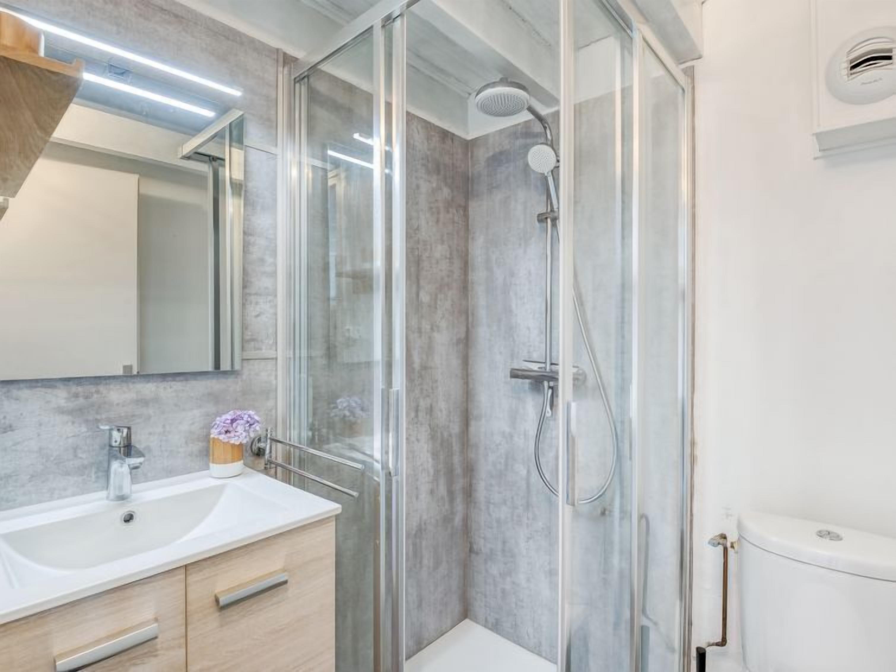 Un baño moderno con ducha envuelta en vidrio, un lavabo blanco y una salpicadera de mármol.