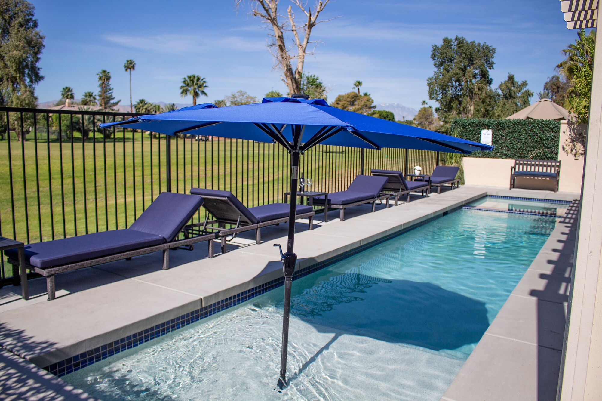 A swimming pool with lounge chairs and a blue umbrella.