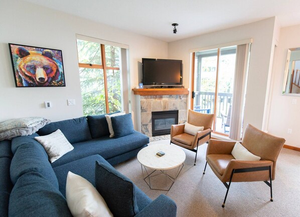 A living room with a sectional sofa, a coffee table, two armchairs, a fireplace, and a television.