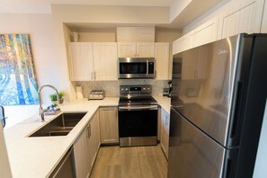 A modern kitchen with stainless steel appliances, light wood cabinets, and a herringbone tile backsplash.