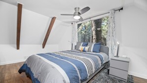 A bedroom with a bed, a nightstand, a ceiling fan, a window with curtains, and a wooden floor. - Vanderhut Chalet - Smart TV, BBQ, Fenced Yard (Sugarloaf)