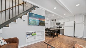 A modern kitchen with white cabinets, a dining area with a wooden table, and a staircase with a metal railing. - Vanderhut Chalet - Smart TV, BBQ, Fenced Yard (Sugarloaf)