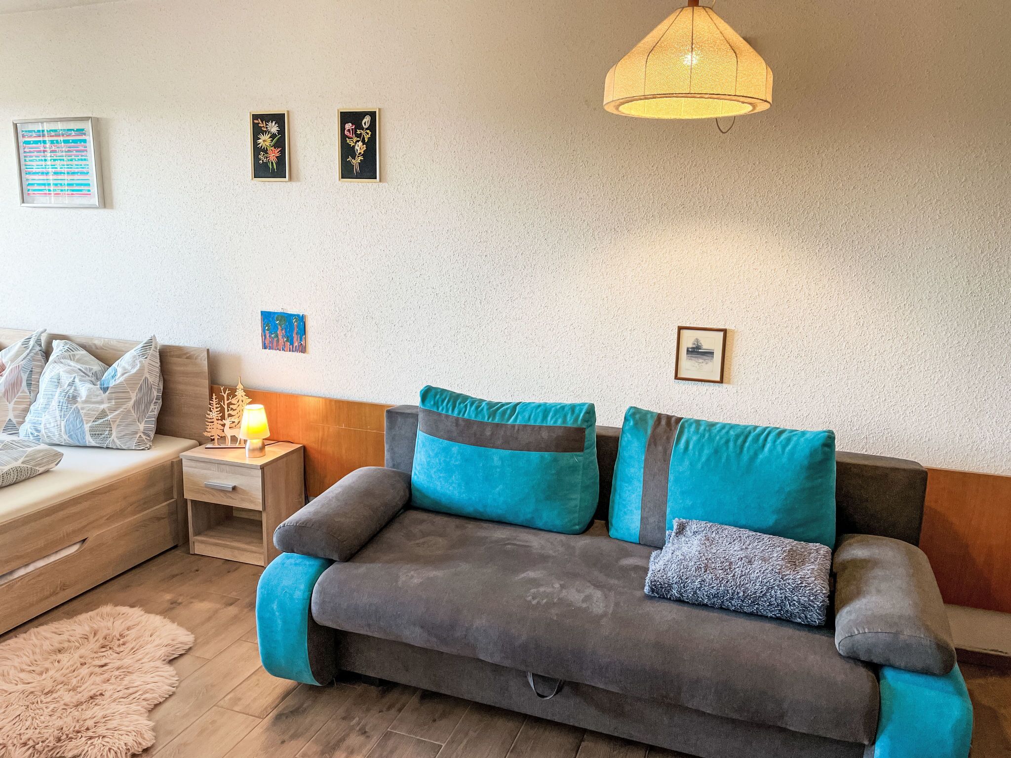 Una sala de estar moderna con un sofá gris, cojines turquesa, una mesita de madera con una lámpara y cuadros en la pared.