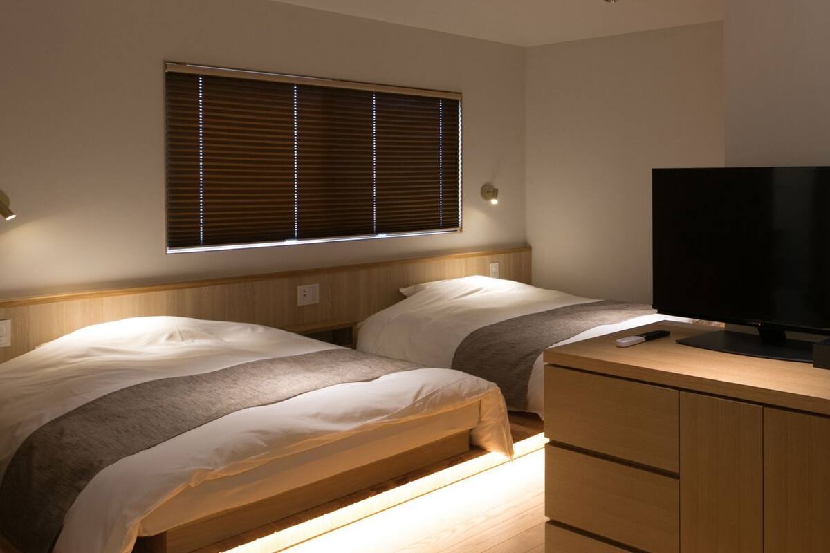 Ein Schlafzimmer mit zwei Betten, einem Fernseher und einem Fenster mit Jalousien.