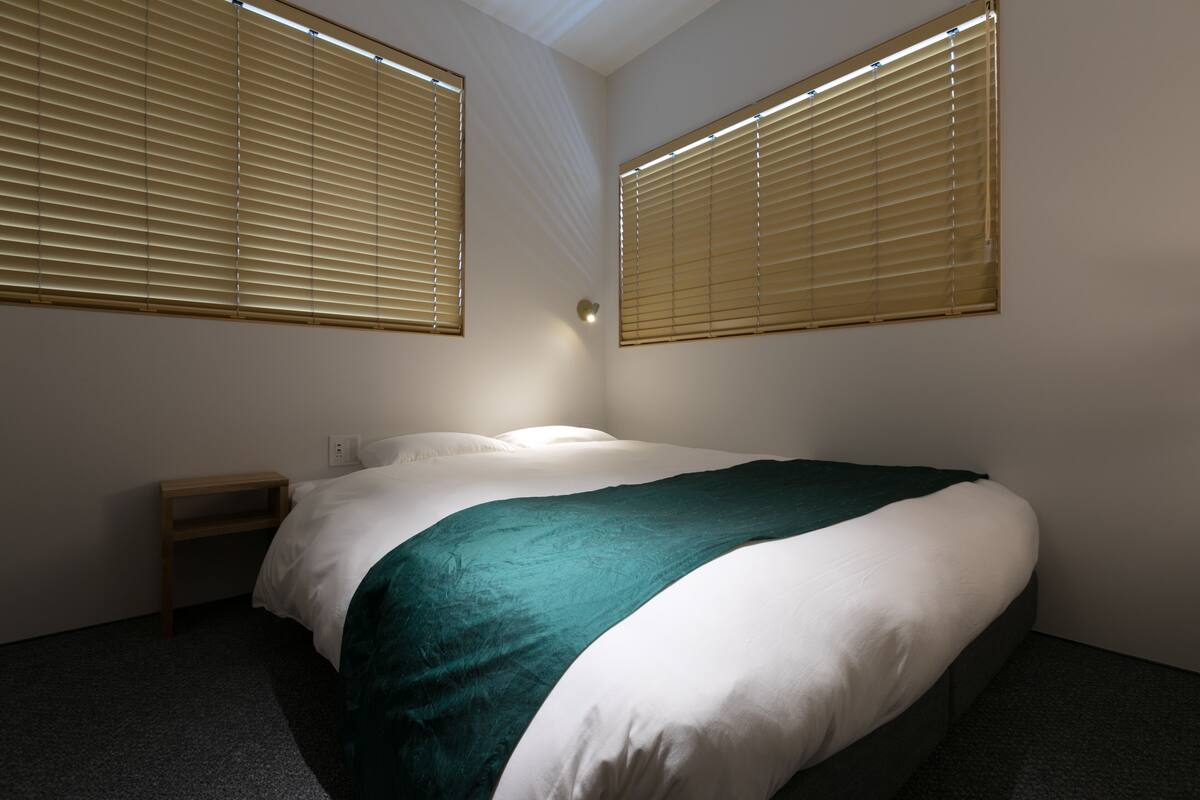 Ein Schlafzimmer mit einem Bett, zwei Nachttischen und zwei Fenstern mit Jalousien.