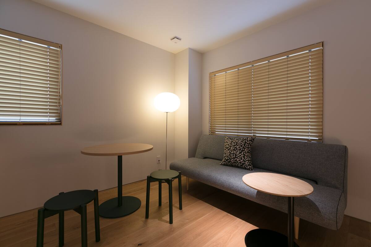 Ein kleines, modernes Wohnzimmer mit einem grauen Sofa, zwei runden Tischen und einer Stehlampe.