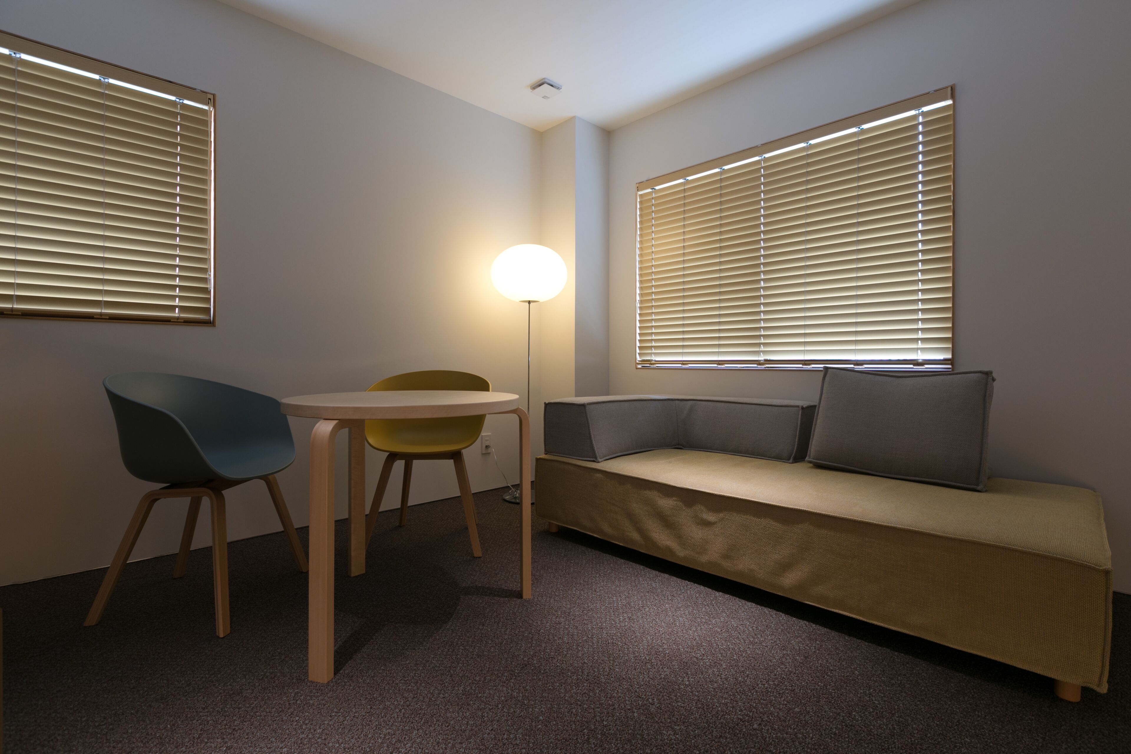 A room with a sofa, two chairs, a table, and two windows with blinds.
