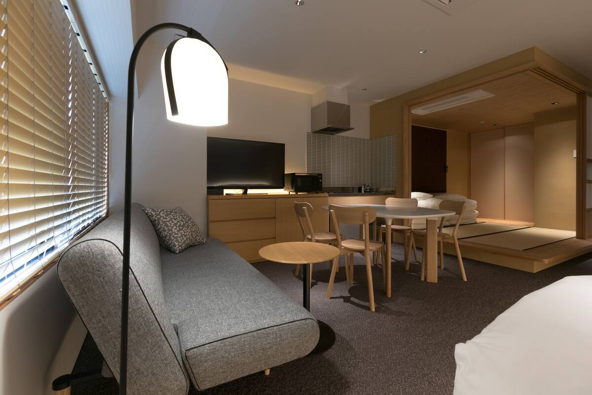 Ein modernes Hotelzimmer mit einer Couch, einem Esstisch mit Stühlen, einem Fernseher und einer Küchenzeile.