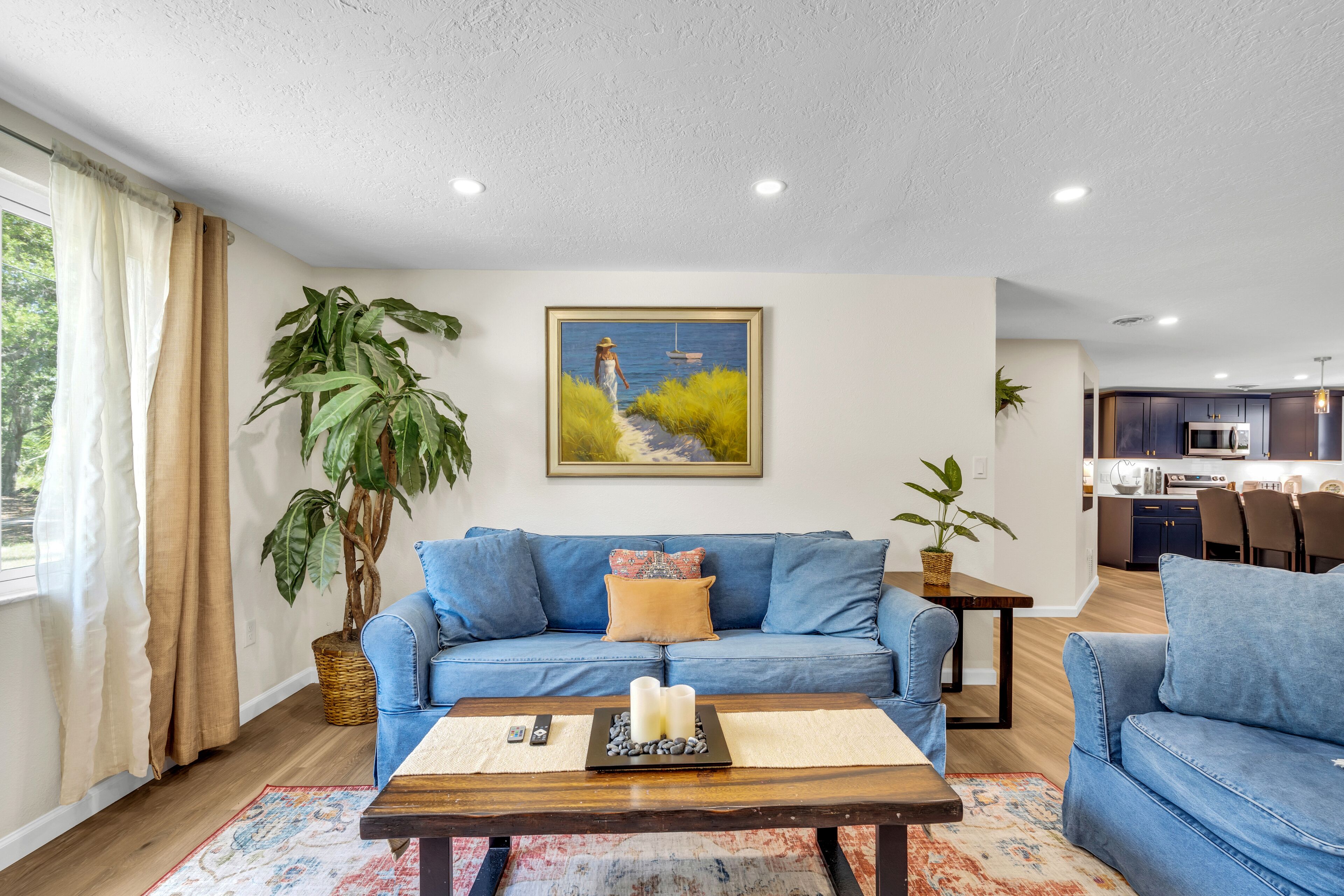 A living room with a blue sofa, a coffee table with candles, and a painting of a woman by the sea.