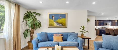 A living room with a blue sofa, a coffee table with candles, and a painting of a woman by the sea.