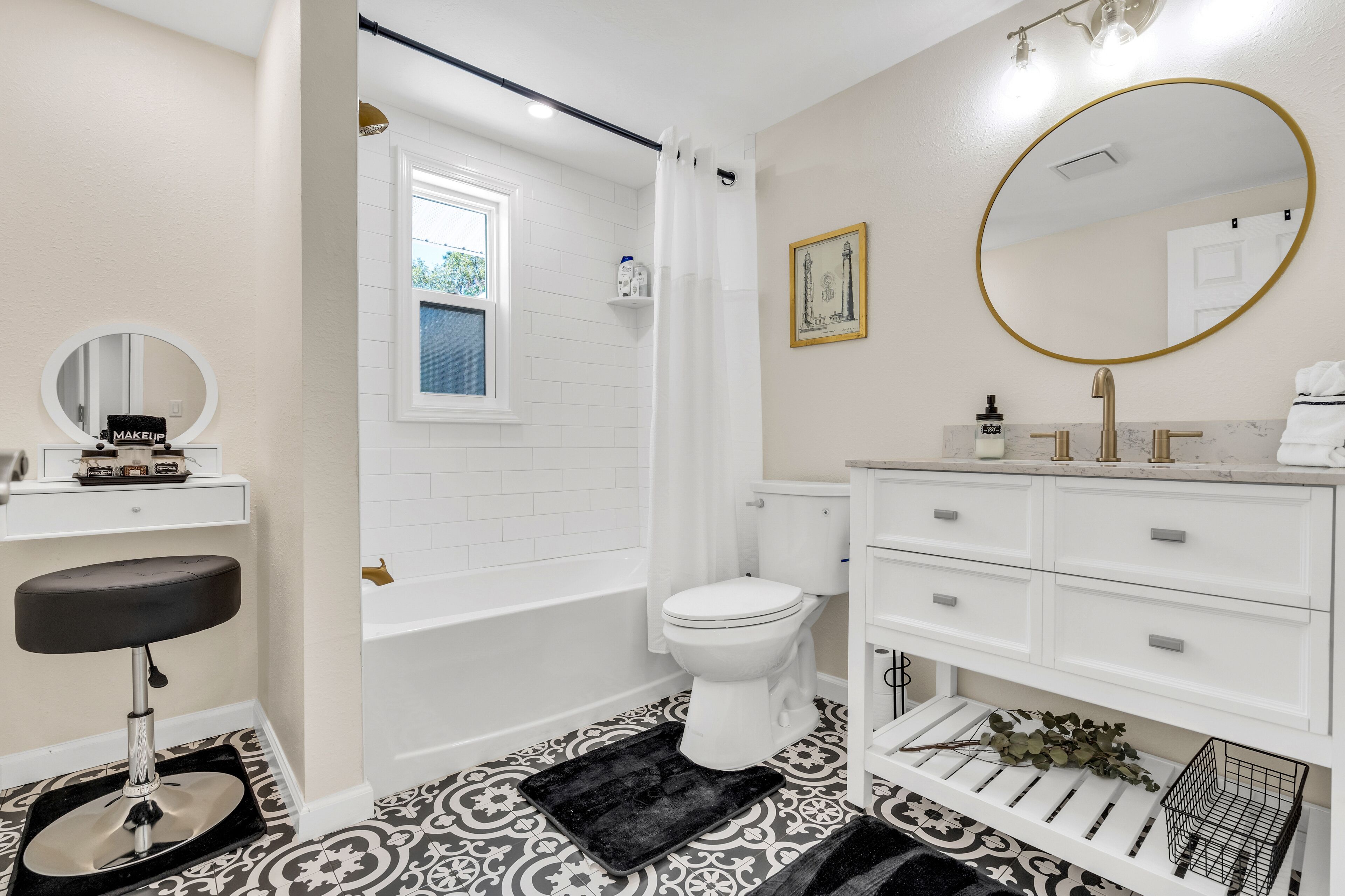 Un baño con inodoro blanco, bañera, tocador con espejo y piso con estampado blanco y negro.
