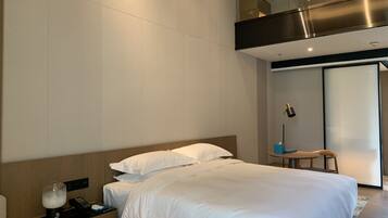 Una habitación de hotel moderna con una cama grande, una mesita de noche con lámpara y una pequeña mesa con teléfono y caja de pañuelos.