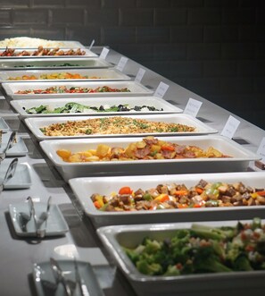 Una lunga tavola imbandita con un buffet assortito, tra cui insalate, pasta e carni.