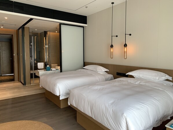 A modern hotel room with two beds, a glass shower enclosure, and pendant lighting. - Courtyard By Marriott Pinghu (Jiaxing)