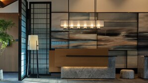 Un interior moderno con una amplia recepción de tonos oscuros, una lámpara minimalista y un gran ventanal con vistas al cielo.