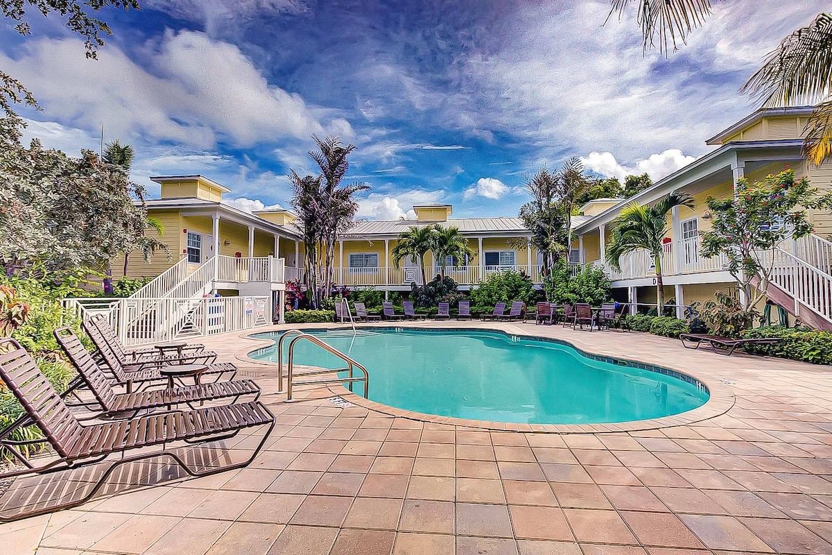 A pool area with lounge chairs, a swimming pool, and a building with a porch.