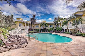 A pool area with lounge chairs, a swimming pool, and a building with a porch.