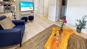 A modern living room with a blue sofa, a wooden coffee table with a vase and wine glasses, and a television displaying a beach scene. - Beach Club | Renovated Condo | Steps to Crescent Beach | Heated Pool & Hot Tub | Siesta Key (Sarasota)