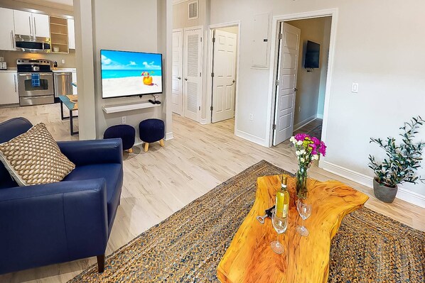 Ett modernt vardagsrum med en blå soffa, ett träbord med en vas med blommor och en platt-TV på väggen.