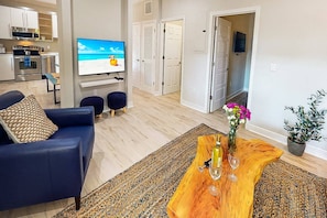 Een moderne woonkamer met een blauwe bank, een houten salontafel en een televisie waarop een strand te zien is.