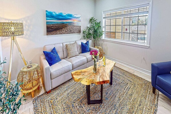 A living room with a sofa, coffee table, and a painting of a beach scene.