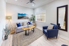A living room with a sofa, a blue armchair, a coffee table, a painting, a floor lamp, and a window with blinds. - Beach Club | Crescent Beach | Pool & Hot Tub (Sarasota)