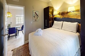 A hotel room with a bed, a desk, chairs, a wardrobe, and a painting on the wall.