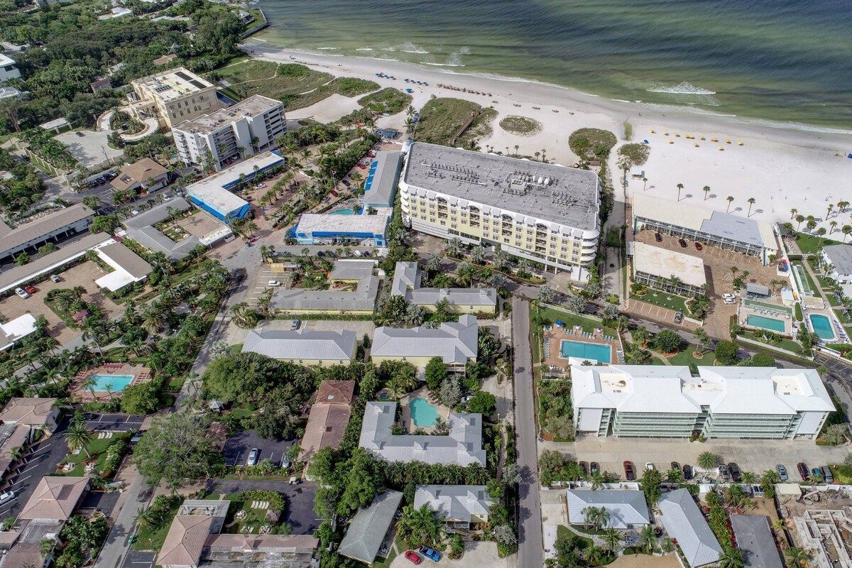 Vue aérienne d’un complexe hôtelier situé sur la côte, avec plusieurs bâtiments, une plage et une piscine.