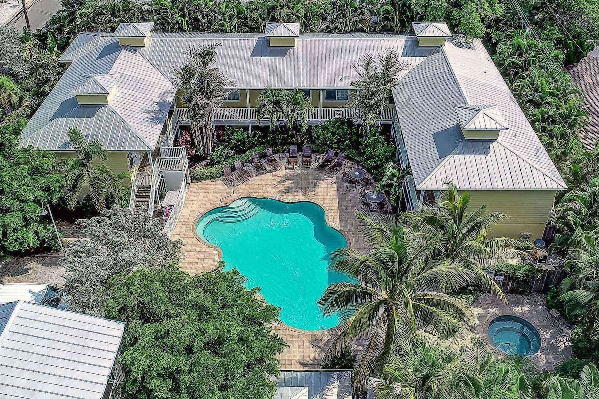Un grande edificio con numerosi balconi, una piscina e rigogliosa vegetazione tropicale.