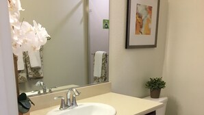 Une salle de bain avec un lavabo blanc, des meubles de couleur brun foncé, un miroir, des toilettes et un tableau encadré au mur.