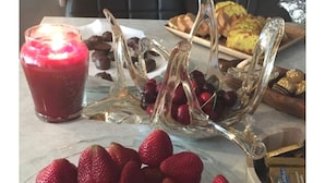 Une table mise pour le petit-déjeuner avec une assiette de fraises, un verre de jus rouge et un pichet en verre contenant des fraises et des cerises enrobées de chocolat.