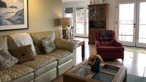 Un salon avec un canapé beige, un fauteuil rouge, une table basse en verre ornée d’un vase de fleurs, un tableau encadré accroché au mur et un meuble en bois.