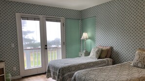 Une chambre avec deux lits, une fenêtre avec des stores, une table de chevet avec une lampe et une vue sur l’extérieur.