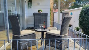Eine Terrasse im Freien mit Korbmöbeln, einem kleinen Tisch mit zwei Weingläsern und einer Flasche, sowie einer Steinmauer.