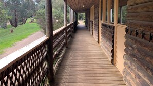 Een houten blokhut met een overdekte veranda en uitzicht op een grasveld met bomen.