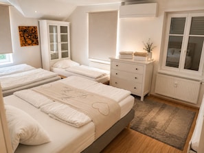 A bedroom with three beds, a white dresser, a radiator, and a window with blinds. - A peaceful natural oasis with woods and a stream—near Basel, Colmar, and Europa-Park (Basel)