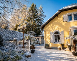 A yellow house with a snow-covered garden and a clear sky. - A peaceful natural oasis with woods and a stream—near Basel, Colmar, and Europa-Park (Basel)