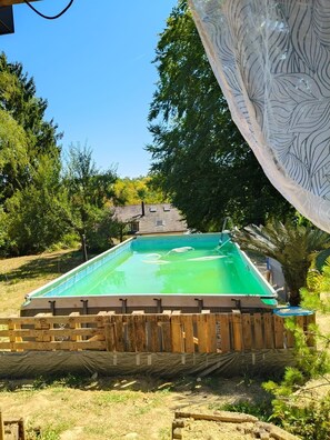 A rectangular swimming pool with a wooden deck surrounding it, set in a landscaped garden with trees and a clear sky.