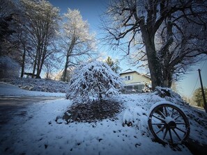 A snow-covered landscape with a house, trees, and a wooden cart wheel.