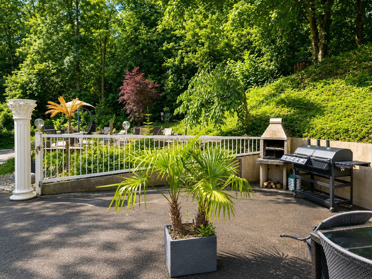 An outdoor patio area with a grill, seating, and a potted plant.