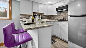 A modern kitchen with white cabinets, a granite countertop, and a stainless steel refrigerator. - Suite at House of L (Chelsea)