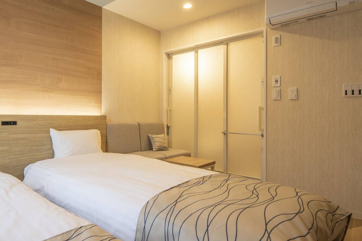 Une chambre d’hôtel avec deux lits, une table de chevet, une armoire et un climatiseur fixé au mur.