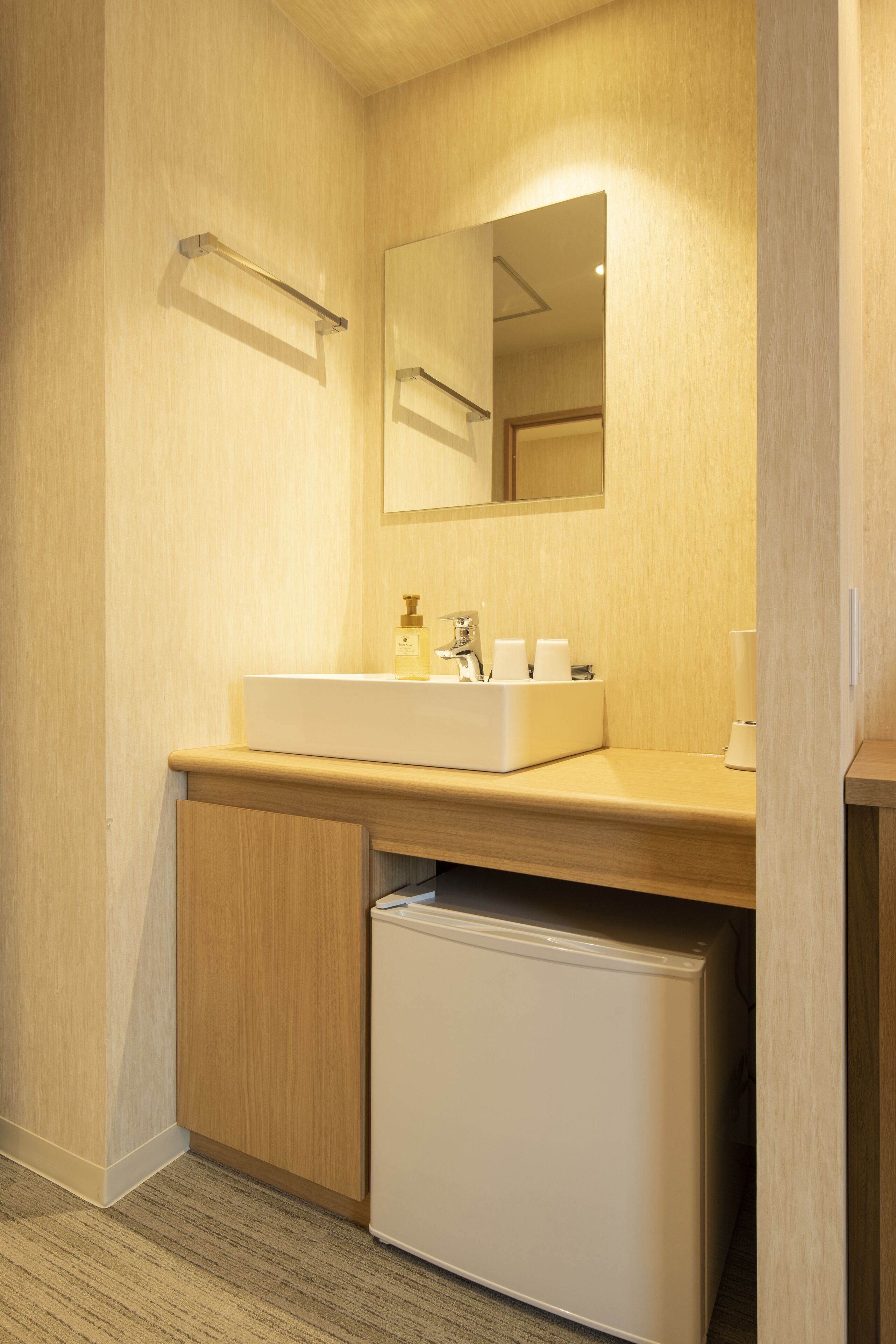 A compact bathroom with a white sink, mirror, and a small refrigerator.