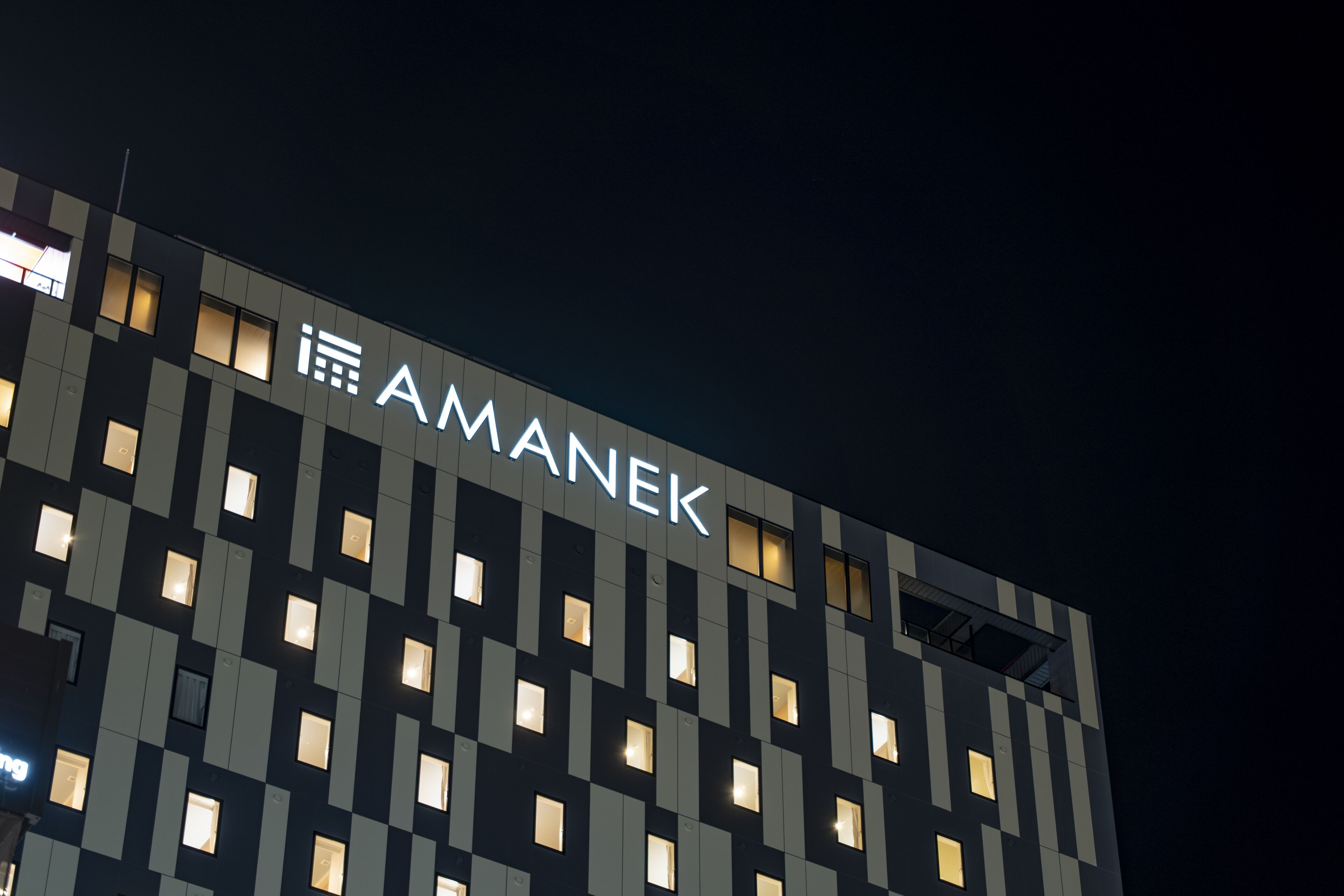 Ein Gebäude, auf dessen Fassade der Schriftzug "AMANEK" leuchtet.