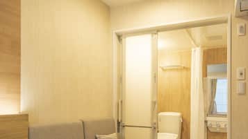 A hotel room with a bed, a sofa, a small table, a bathroom with a toilet and shower, and a wooden wall.