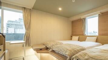 A modern hotel room with two beds, a small desk, and a view of the city.