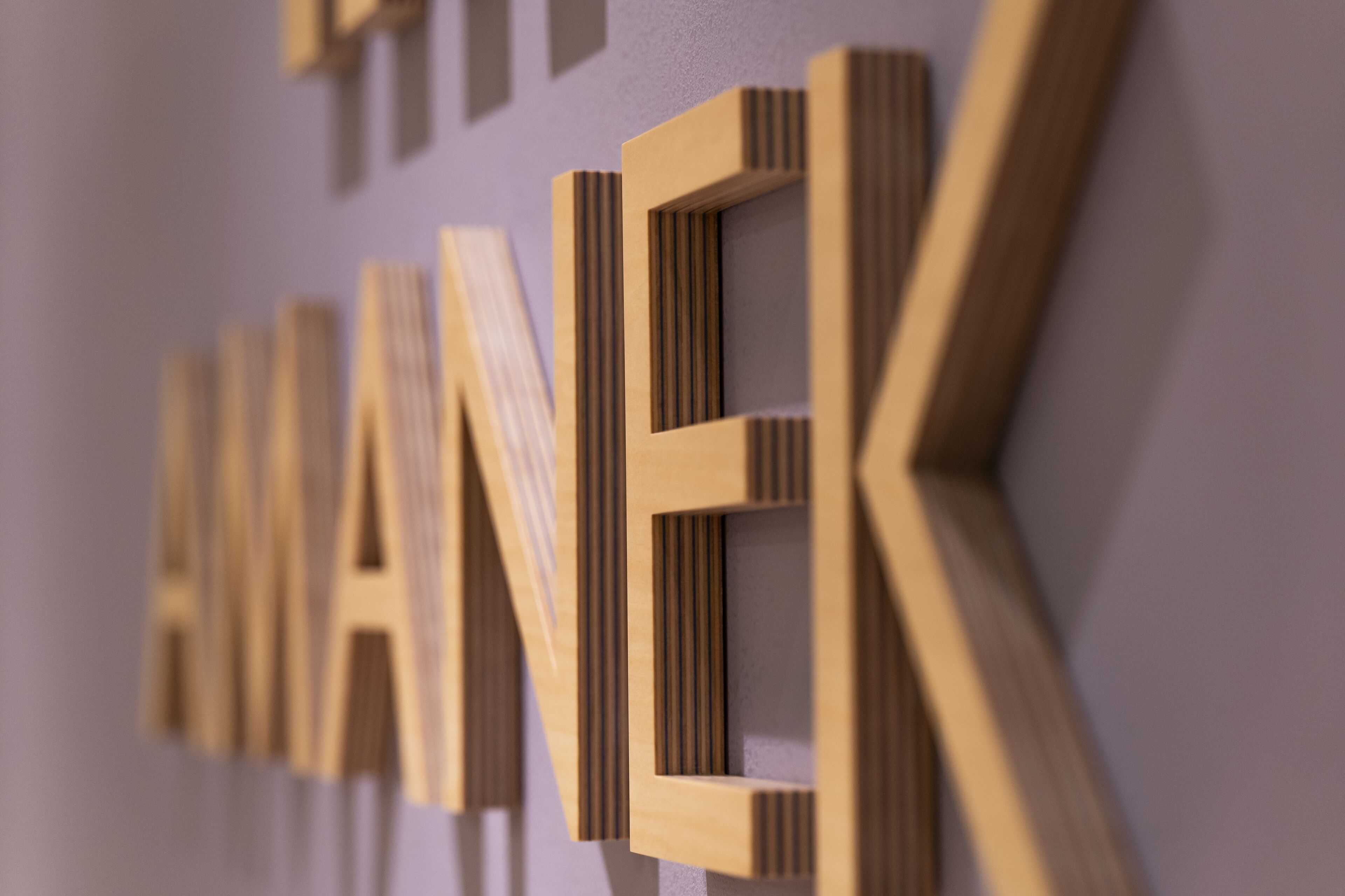 A close-up of wooden letters spelling "MANEK" on a wall.