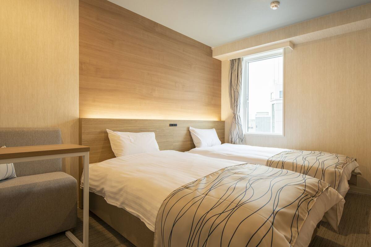 Une chambre d’hôtel avec deux lits, un bureau et une fenêtre.