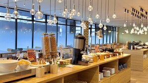 Een ontbijtbuffet met diverse soorten eten, een koffieapparaat en hangende lampen.