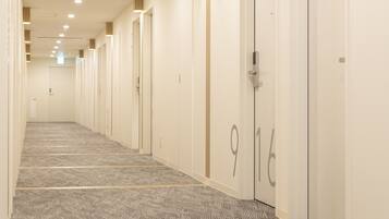 Un pasillo de hotel con puertas numeradas, piso alfombrado e iluminación empotrada.